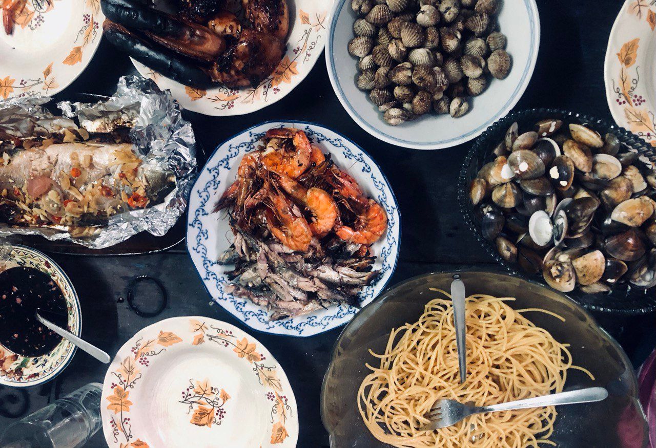 A flatlay image of numerous plates and bowls holding pasta, prawns, fish, clams, blood cockles, mussels and more